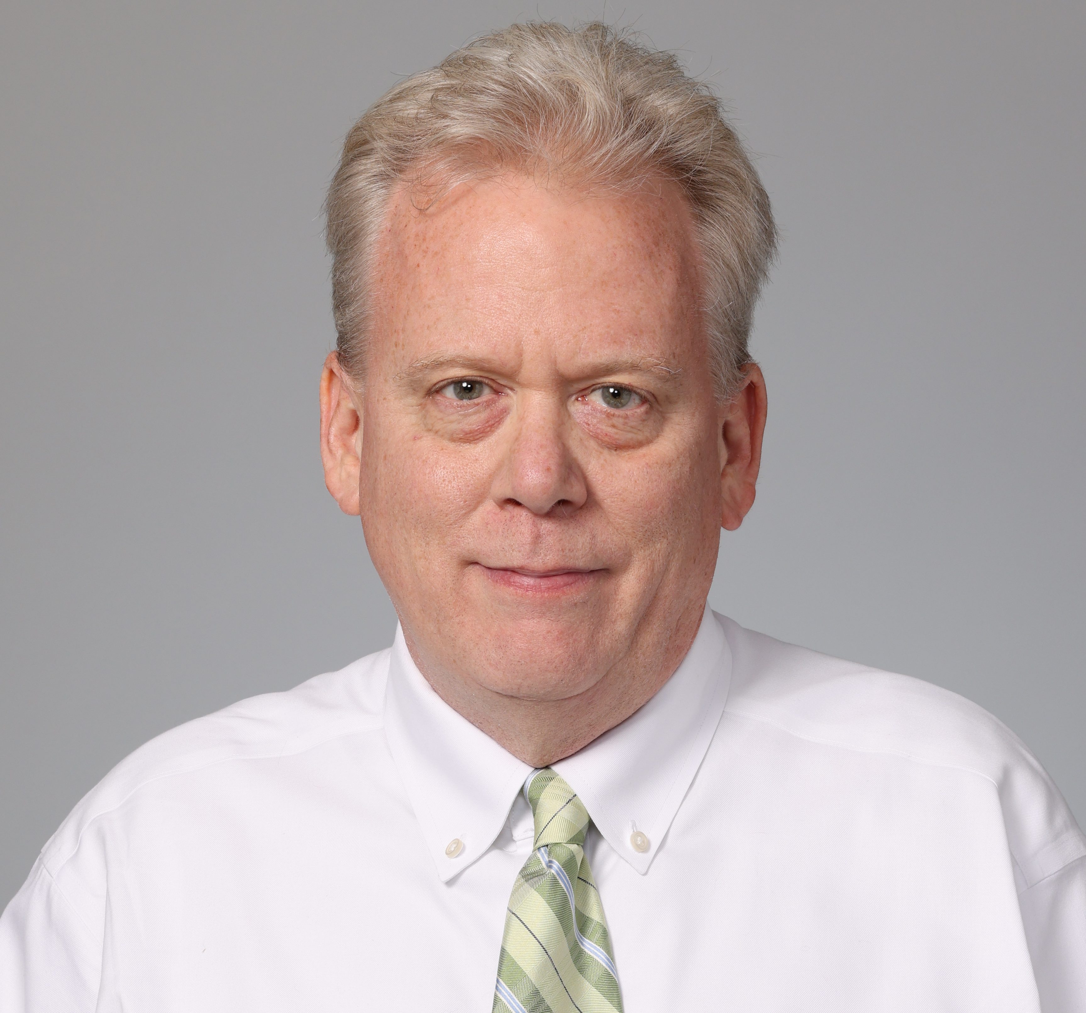 Professional headshot of Bob Monek wearing a white shirt and a light green striped tie, against a plain gray background.